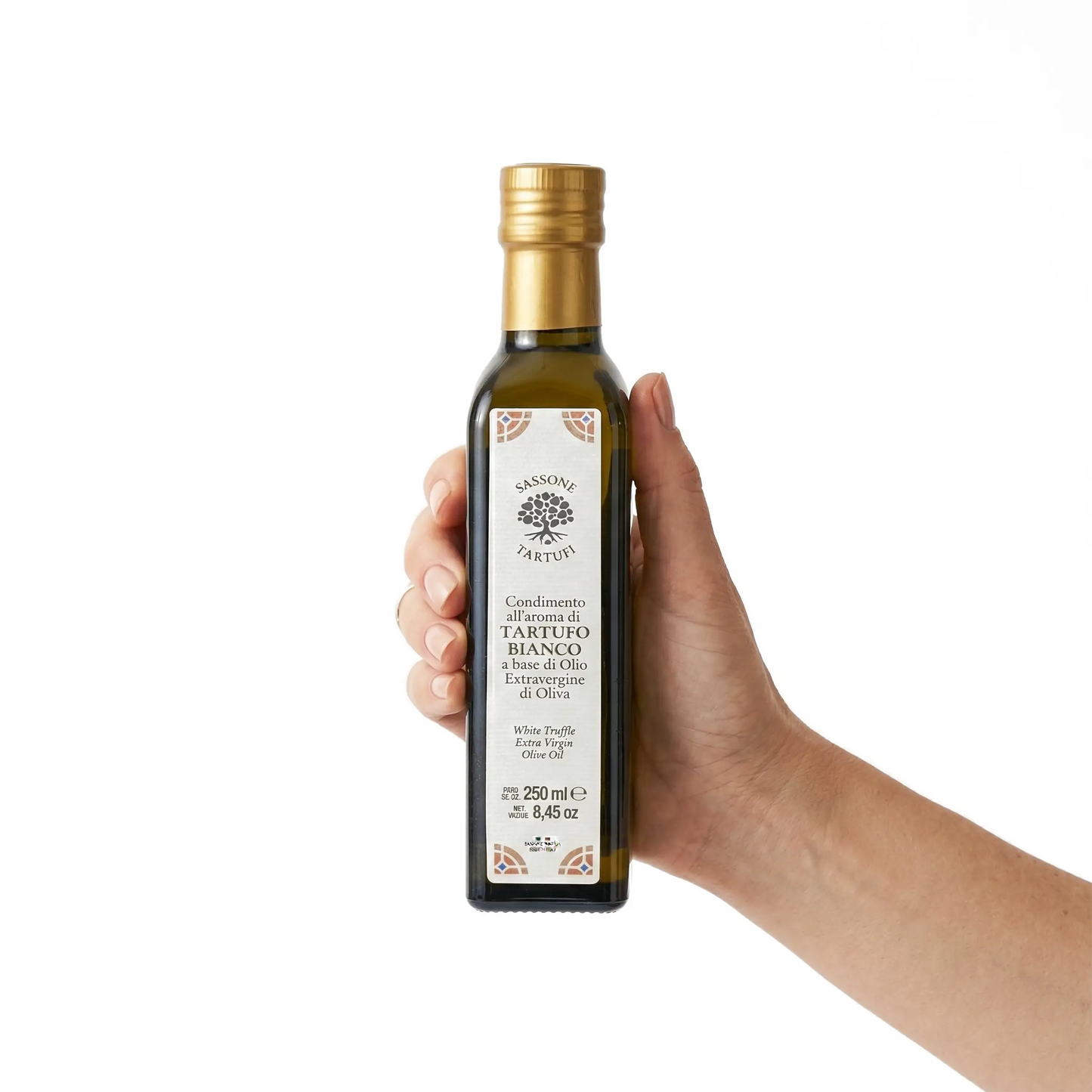 Uma mão feminina segura uma garrafa de azeite de oliva com aroma de trufa branca Sassone Tartufi sobre fundo branco. Demonstração do tamanho do produto de 250ml.