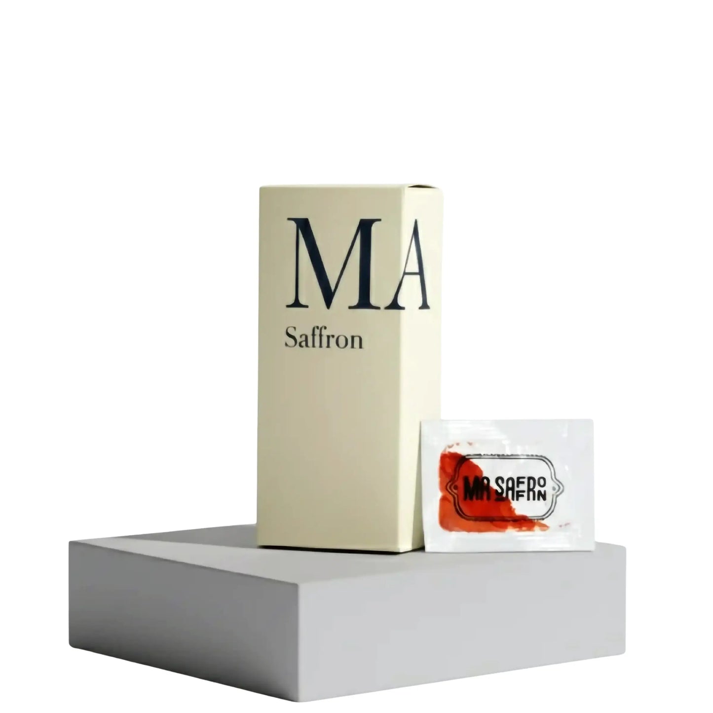 Embalagem minimalista e elegante da marca MA Saffron, apresentando uma caixa vertical de cor creme com o logotipo 'MA Saffron' impresso em letras sofisticadas. Ao lado da caixa, um sachê individual de amostra contendo uma porção de açafrão iraniano premium, destacando a cor vibrante dos pistilos. Ambos os itens estão posicionados sobre um pedestal geométrico cinza-claro, com fundo branco isolado, transmitindo uma imagem de pureza, luxo e design moderno. Esta apresentação ressalta a conveniência e a alta qua