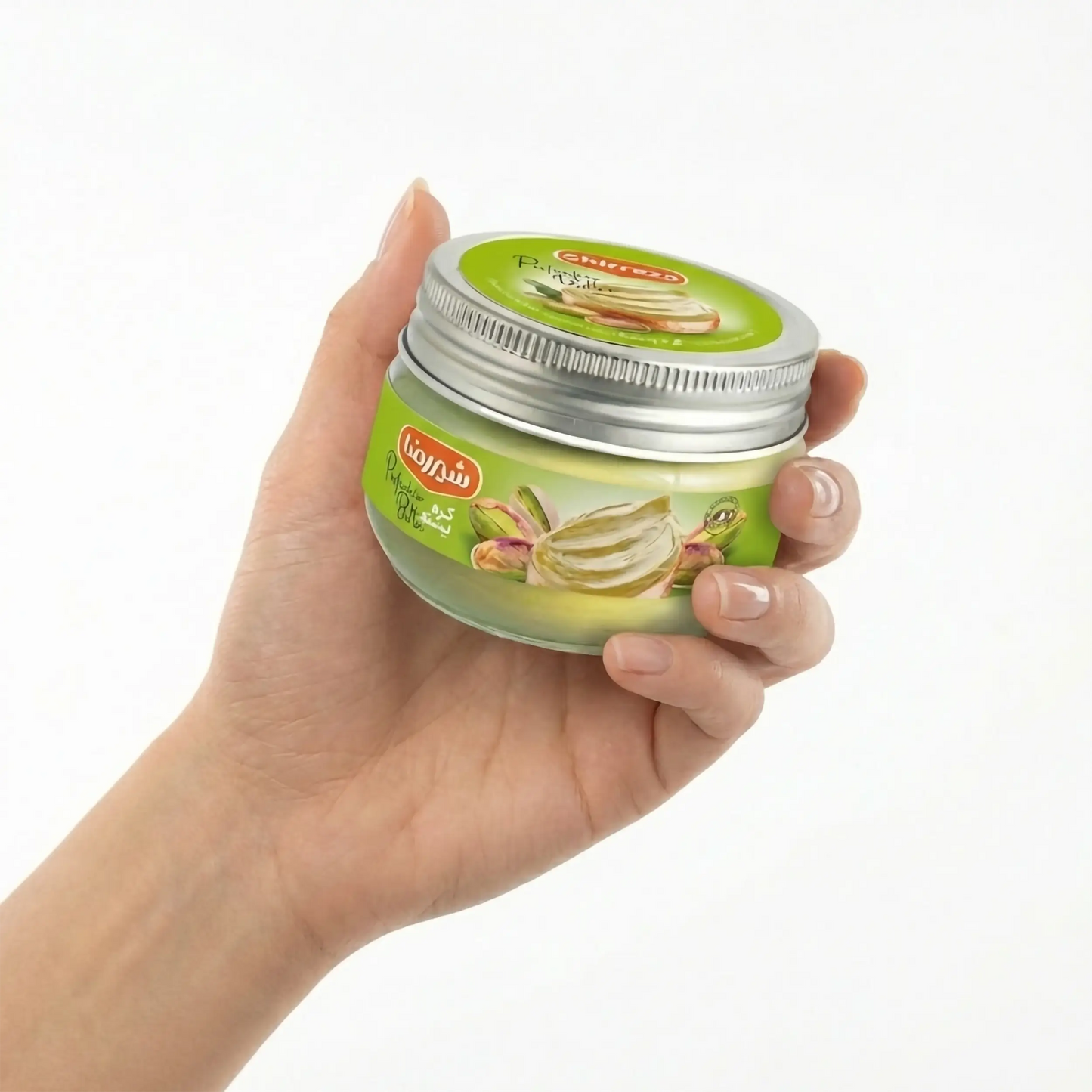 Mão exibindo o frasco de manteiga de pistache Shirreza contra fundo branco. Uma opção gourmet versátil para passar no pão, adicionar a smoothies ou usar em receitas de confeitaria fit.